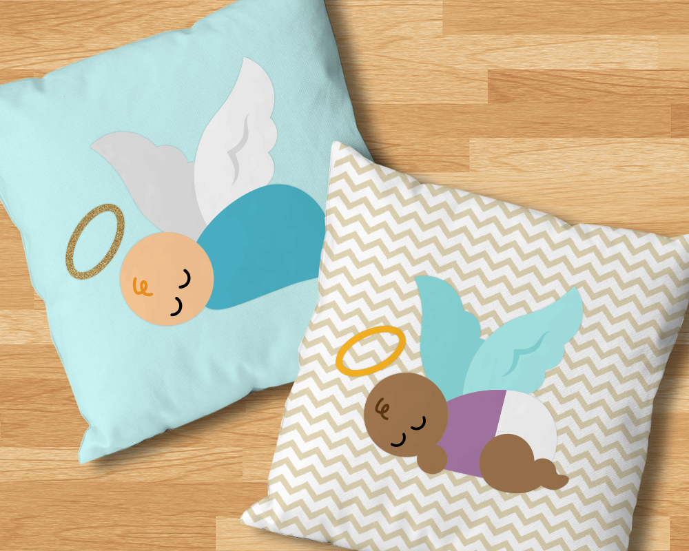 Two throw pillows on a wood background. Each features a sleeping baby with wings and a halo. The left pillow is blue with a white bundled baby. The right pillow is beige and white chevron with a black baby sucking its thumb and wearing a diaper.