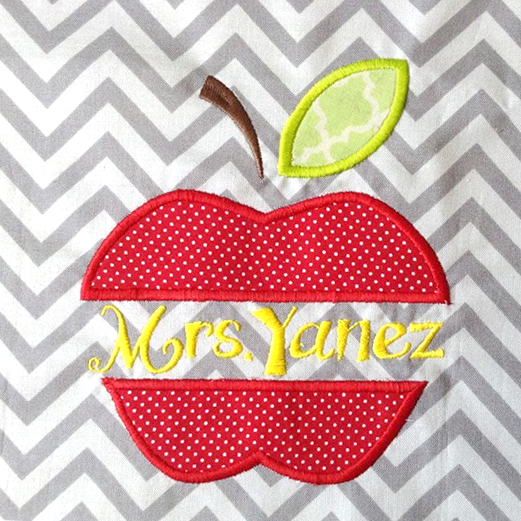 A piece of white and grey chevron fabric has an applique apple with a split in the middle. The customer has added "Mrs Yanez" to the split space. (Text is not included as part of the design).