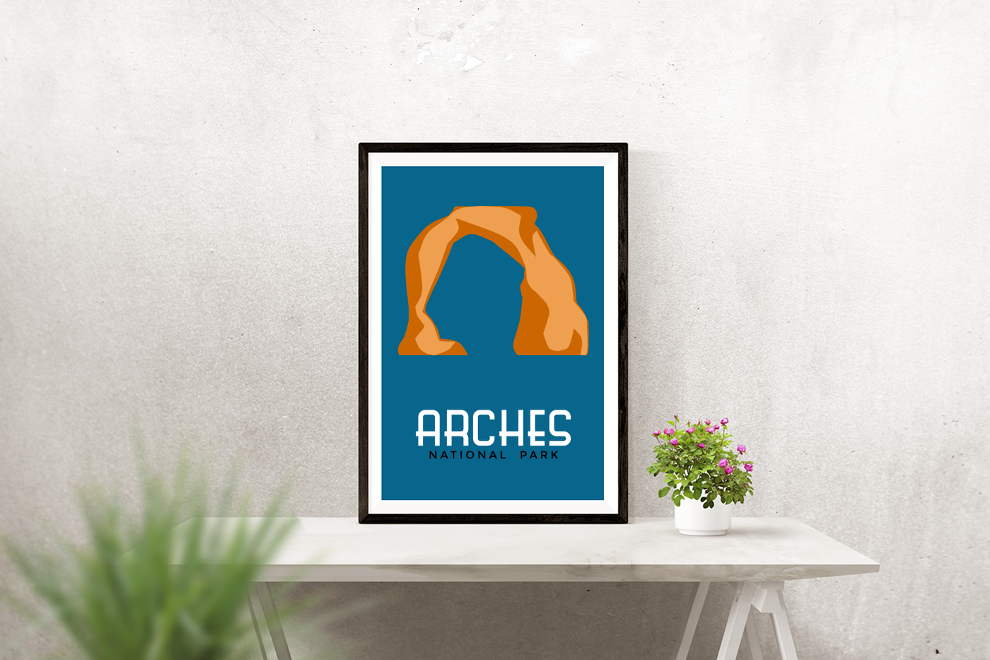 A framed poster on a table. The background is blue and in the center is the Arches rock formation. Below it says "Arches national park."