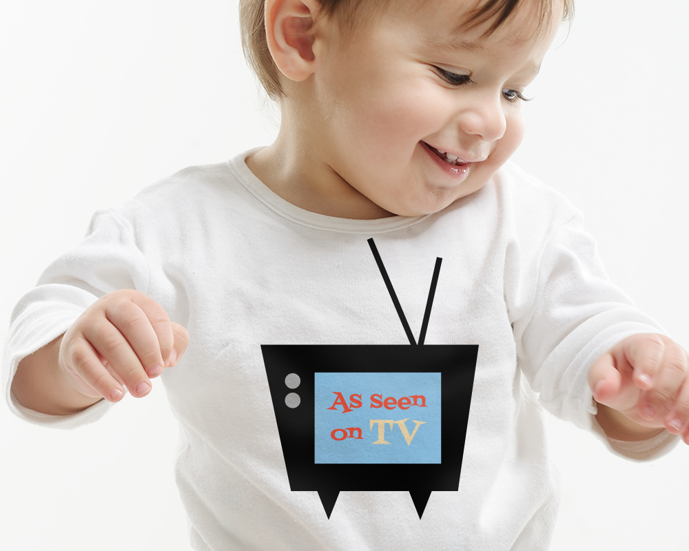 A white baby wearing a long sleeve white shirt. On the shirt is an old-fashioned TV with the words "As seen on TV" in the middle."