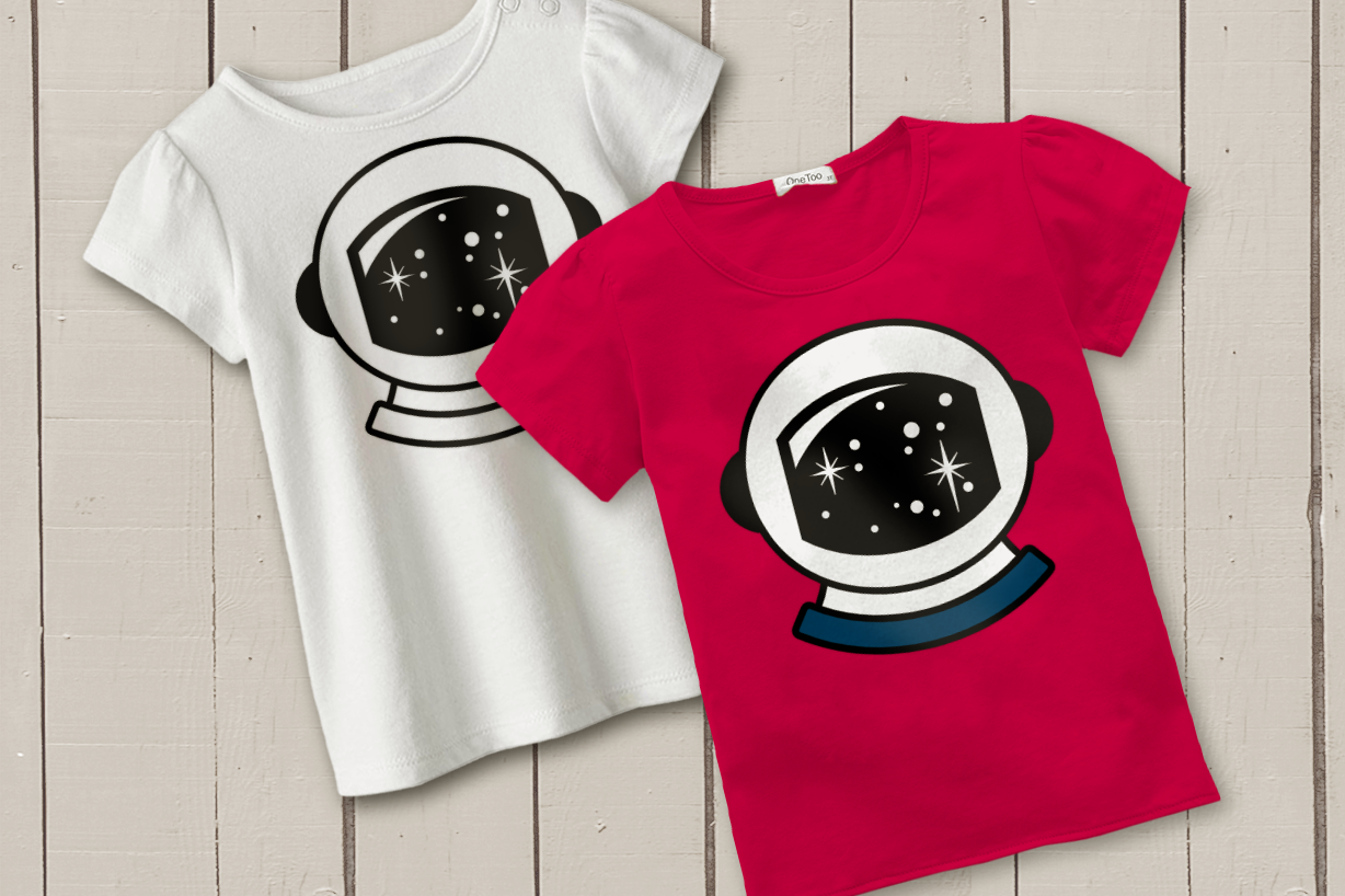 Two children's tees lay on a beige painted wood background. Each shirt has the image of an astronaut helmet with stars reflected in the visor.