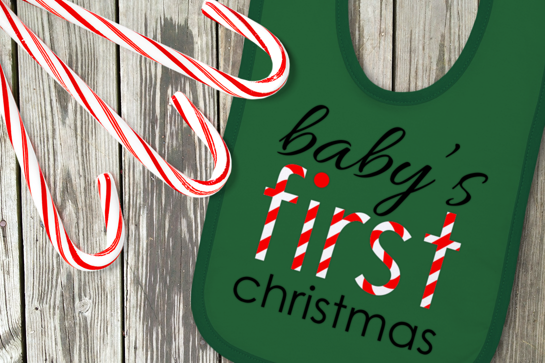 Green bib with the words "baby's first christmas" on it. First is done in candy cane stripes.