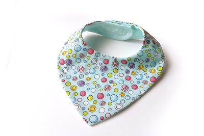 A bandanna style bib sits on a white background. The front bib fabric is aqua with bright dots in many colors and sizes outlined in black. The lining fabric is aqua flannel.