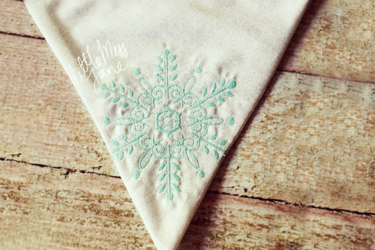 An intricate aqua snowflake embroidery on white triangle bunting flag.