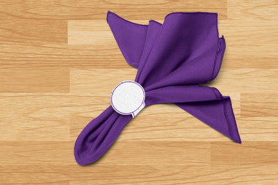 White faux leather napkin ring with a circle is wrapped around a purple napkin on a wooden surface.