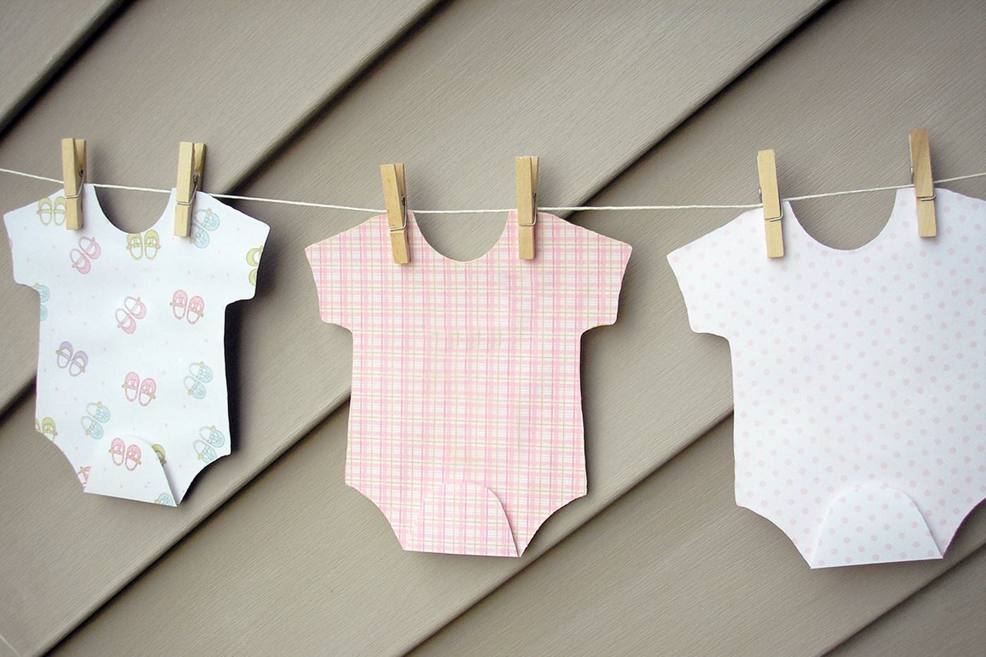 Paper bodysuits in different pastel patterns and colors hanging from a clothesline.