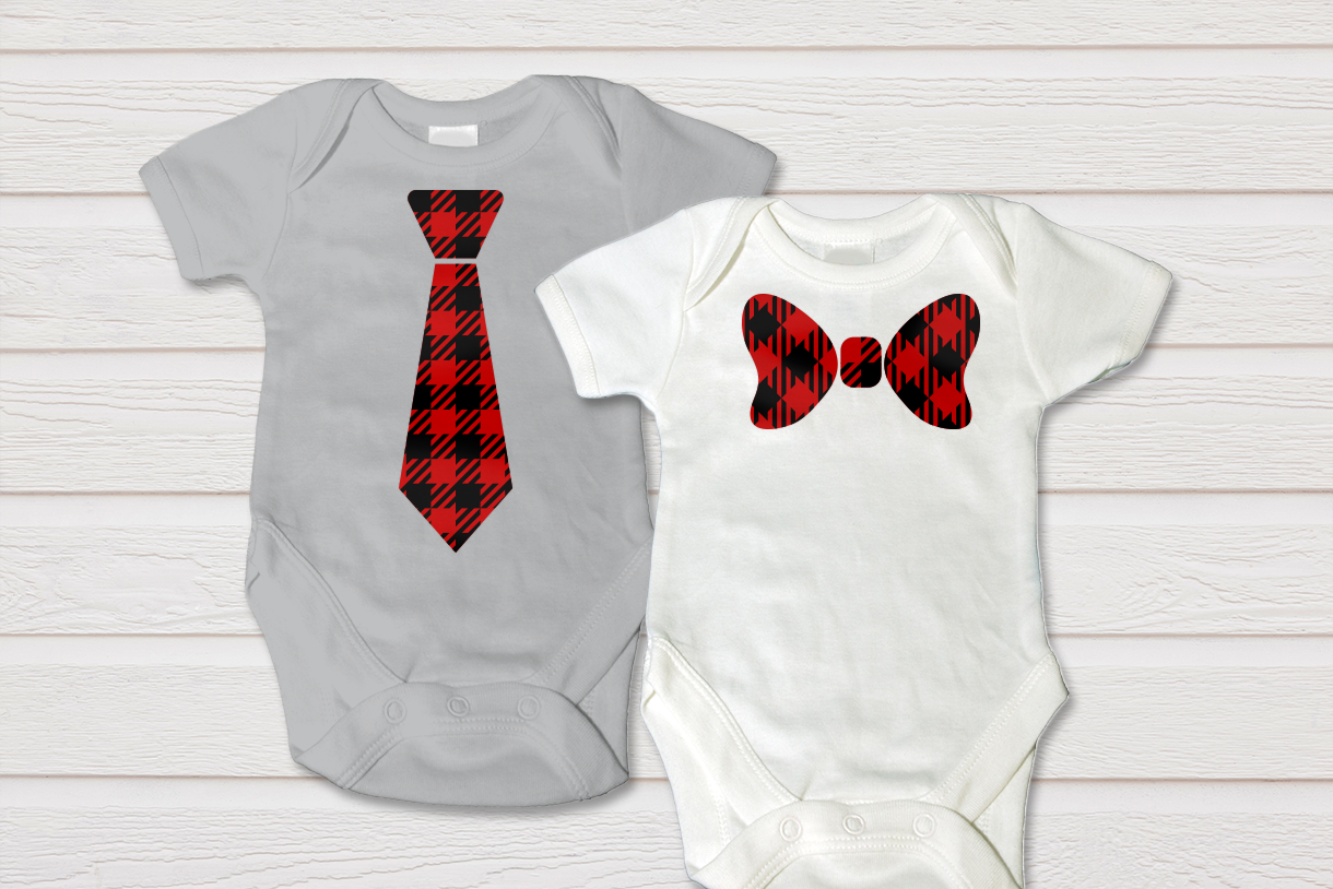 Two baby onesies on a white painted wood background. The left onesie has a neck tie, the right onesie has a bow tie. Both are red and black with a buffalo plaid pattern.