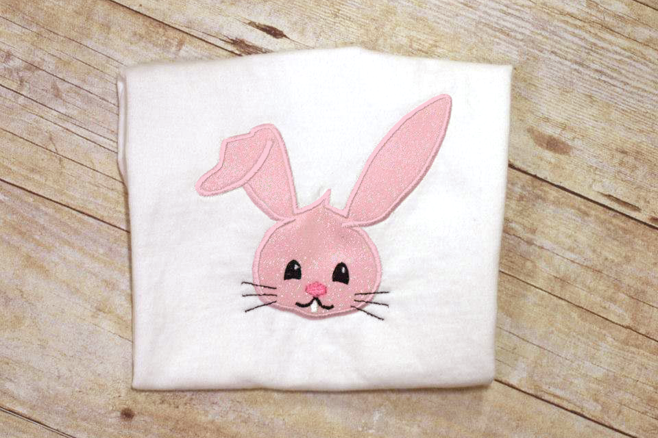 White folded tee with an applique Easter bunny face with one ear flopped over.