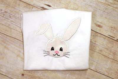 White folded tee with an applique Easter bunny face with one ear flopped over.