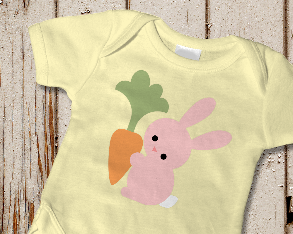 A pale yellow onesie has the design of a pastel pink bunny holding a carrot.