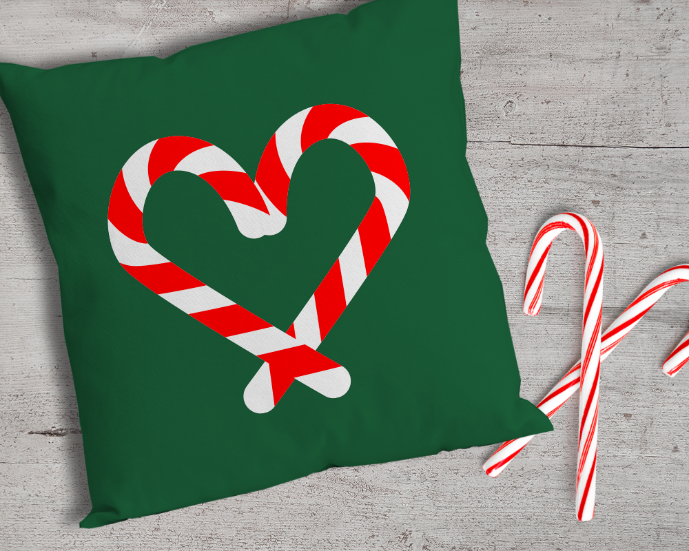 A green throw pillow with two candy canes laying near it. The design on the pillow has two candy canes forming a heart shape.