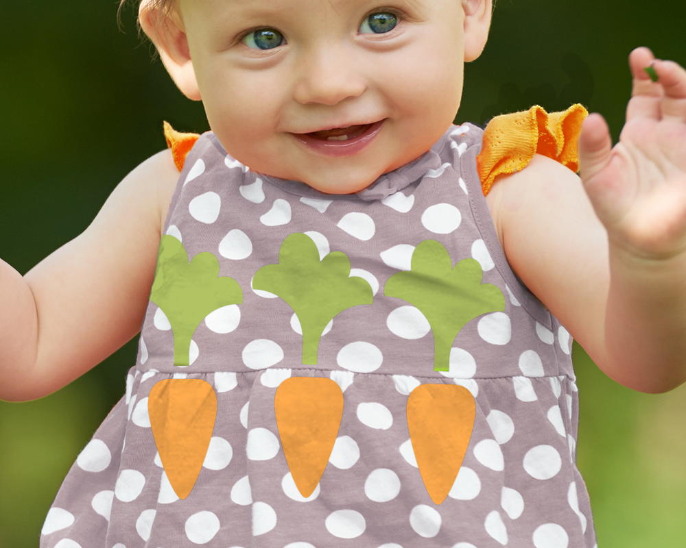 A white baby girl wears a grey and white polkadot dress with orange sleeves. On the dress are 3 cute carrots.