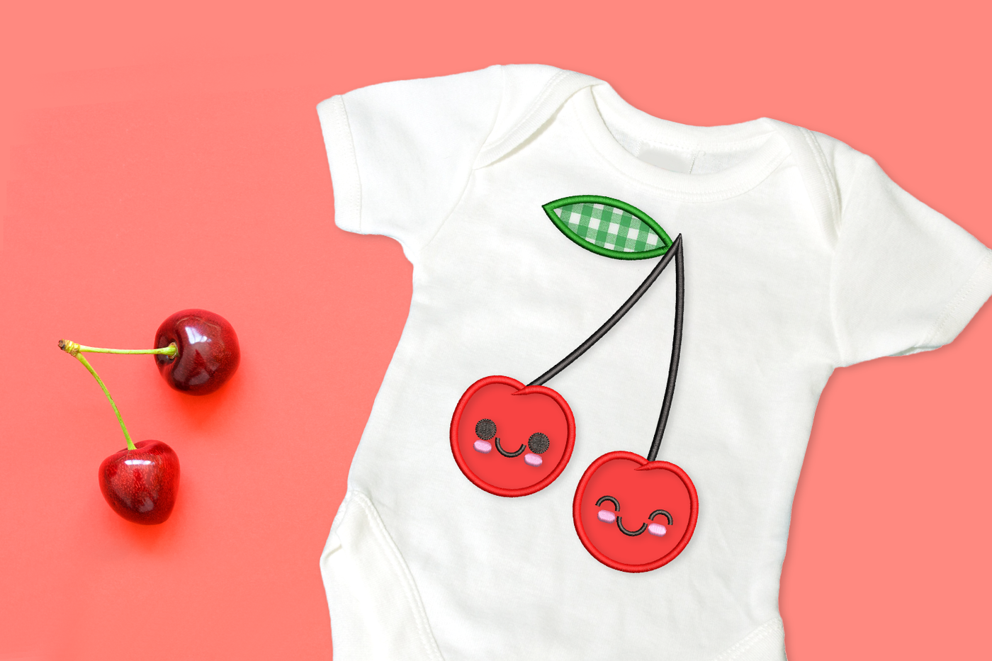 White onesie with applique design of a pair of cartoon cherries on the stem with a single leaf.