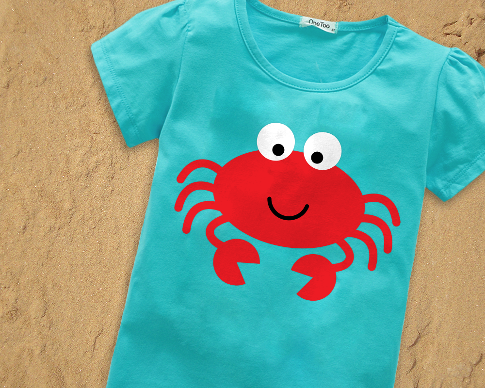 Cute cartoon crab in a turquoise shirt. The shirt lays on a sandy beach.