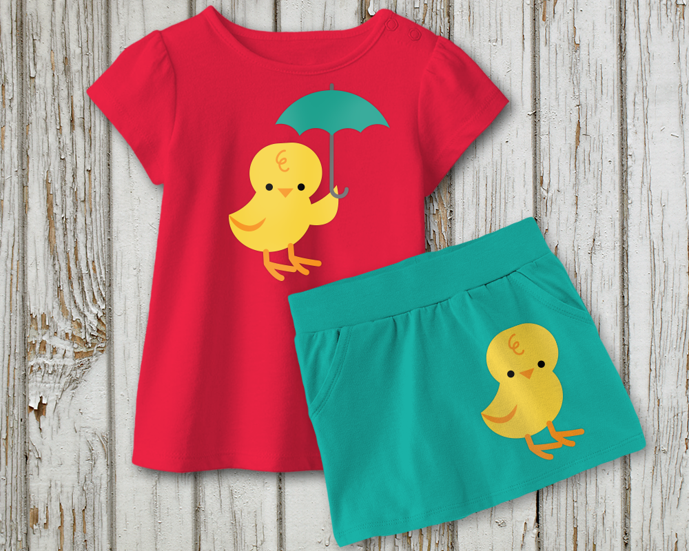 A child's shirt and skirt lay on a weathered wood background. The skirt is turquoise with a baby chick at the bottom right. The shirt is dark pink with a baby chick  holding a turquoise umbrella in the center.