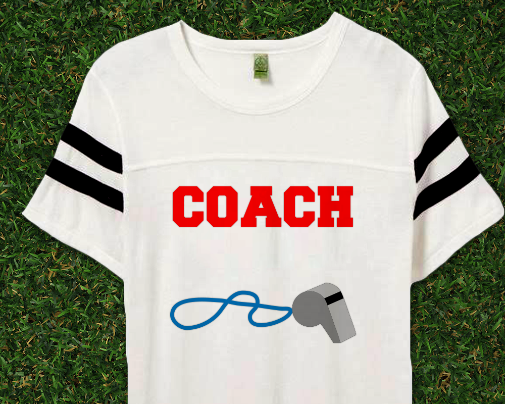 Sports tee laying on some grass. On the shirt it says "Coach" with a whistle.