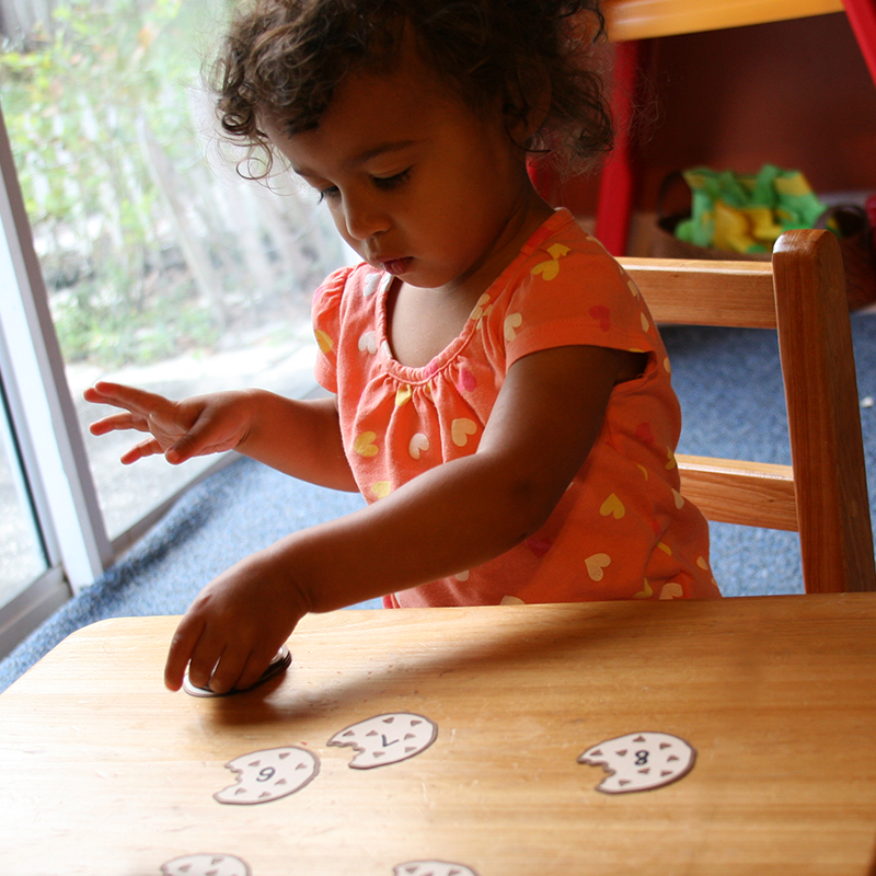 A black toddler girl plays with paper chocolate chip cookies that have numbers on them.