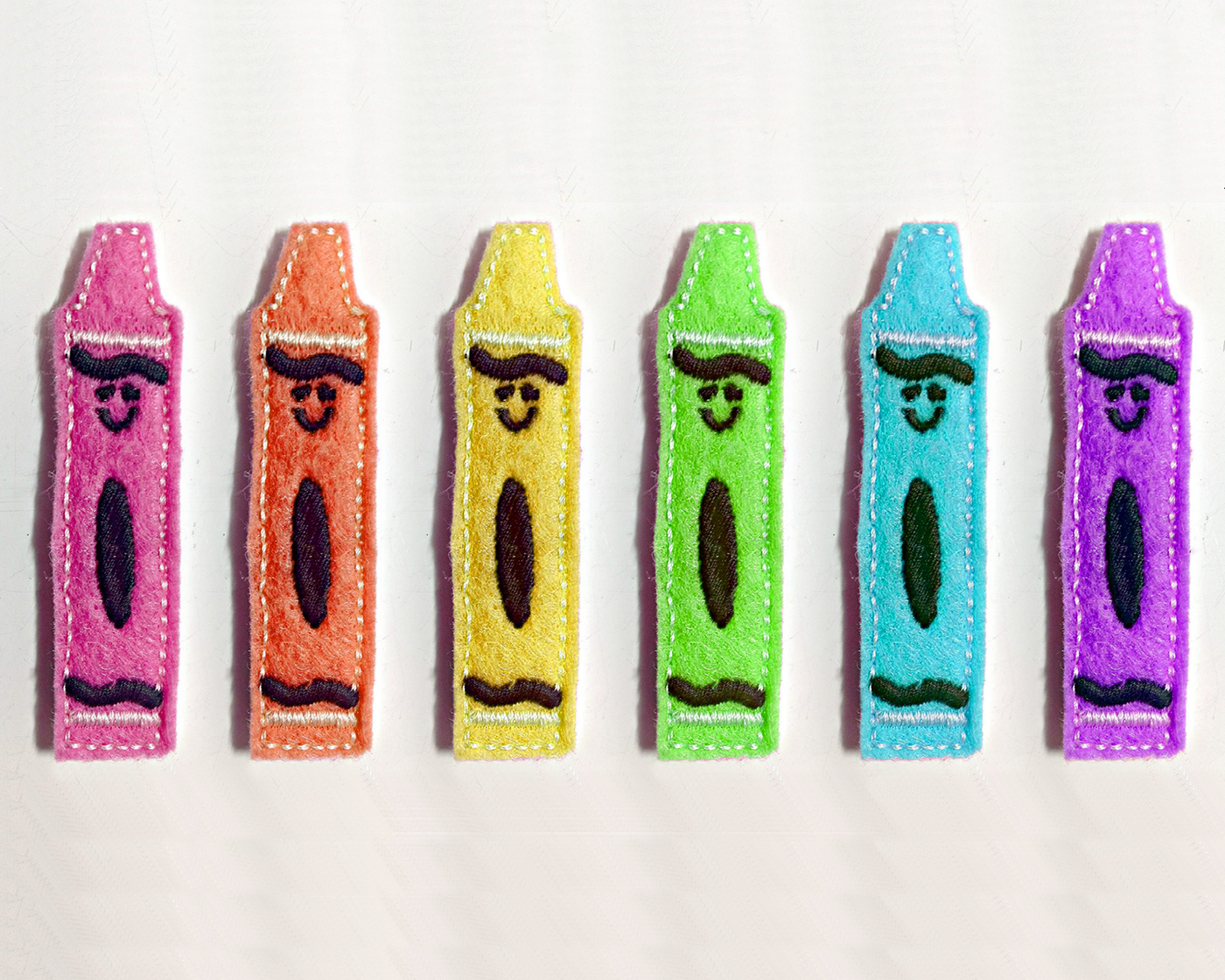 Five smiling crayon felties in a row, each in a different bright color.