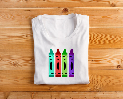 A folded white tee with a design featuring 4 smiling crayons in different colors.