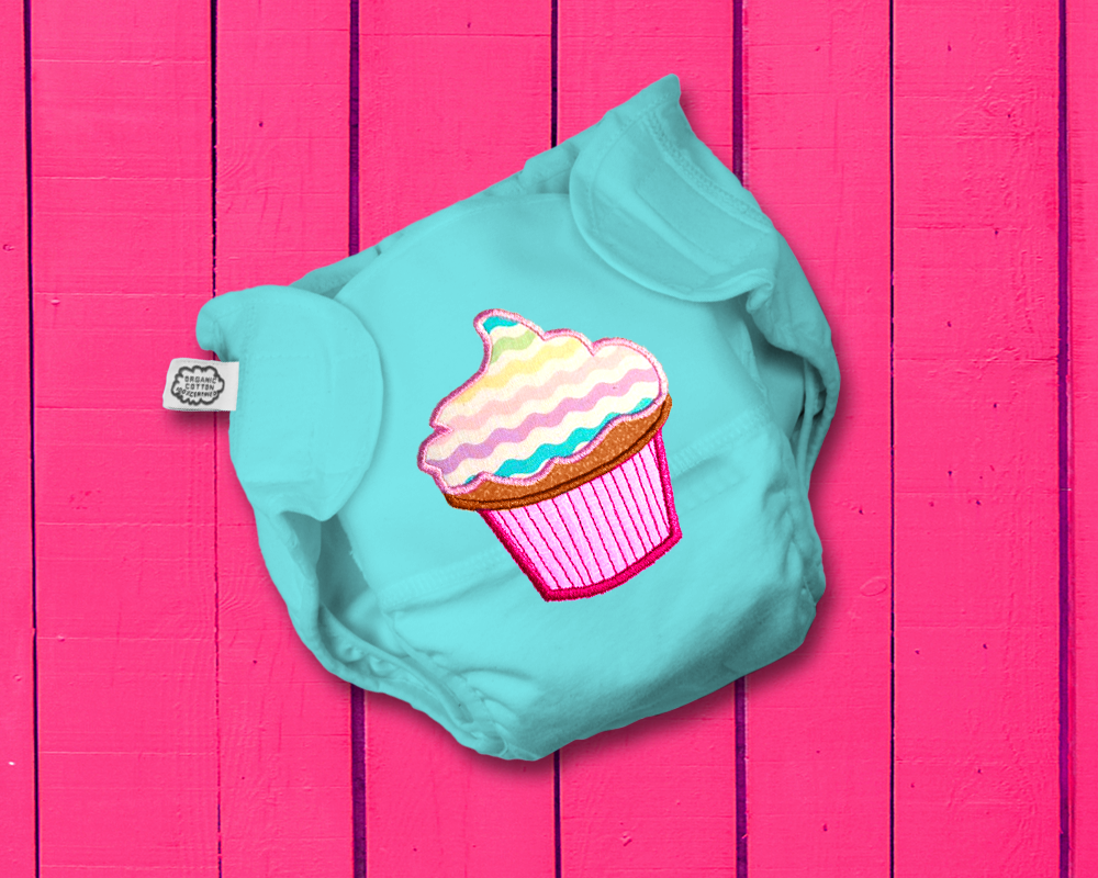 An aqua cloth diaper on a pink wood background. The diaper has an applique of a frosted cupcake.