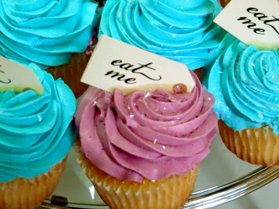 Pink and blue frosted cupcakes with tag toppers that say "eat me"