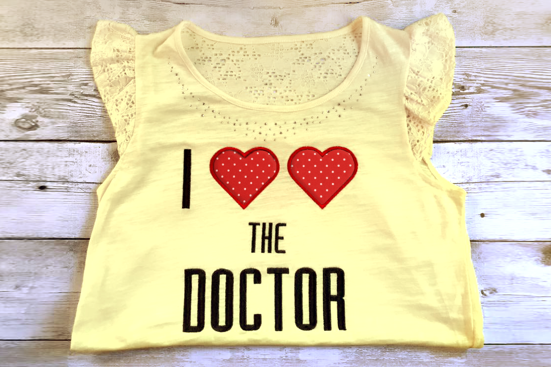 Shirt with embroidered phrase "I heart heart the doctor." The two hearts are applique.