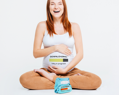Pregnant white woman has a shirt with a loading bar design that says "downloading: baby in progress." In front is a cloth diaper with a loading bar that says "Caution! download in progress."