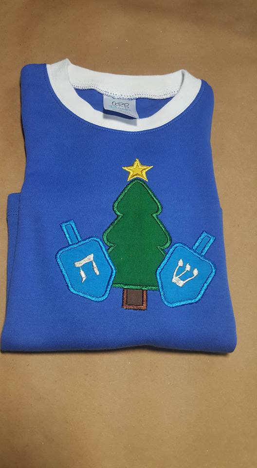 A blue pajama top is decorated with the applique of a Christmas tree with a dreidel on each side.