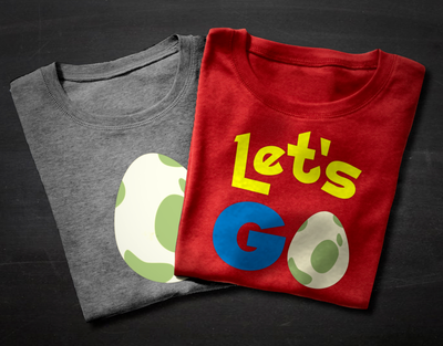 Two folded shirts sit on a chalkboard backdrop. The right shirt says "Let's GO" with a spotted cream and green egg in place of the O. The left shirt has the same egg by itself.