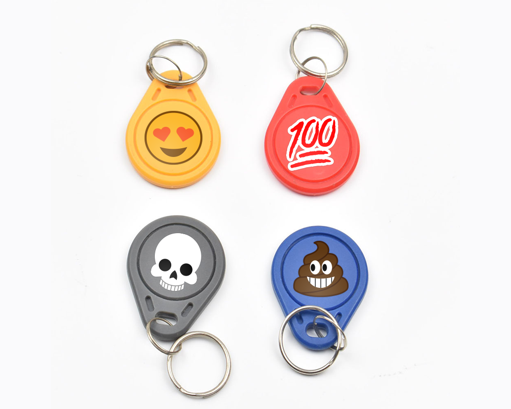 Four key fobs, each decorated with a different emoji: heart eyes, 100, skull, and poop.