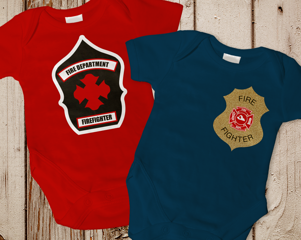 Two baby onesies. One has a fire fighter badge, the other has a fire fighter shield.