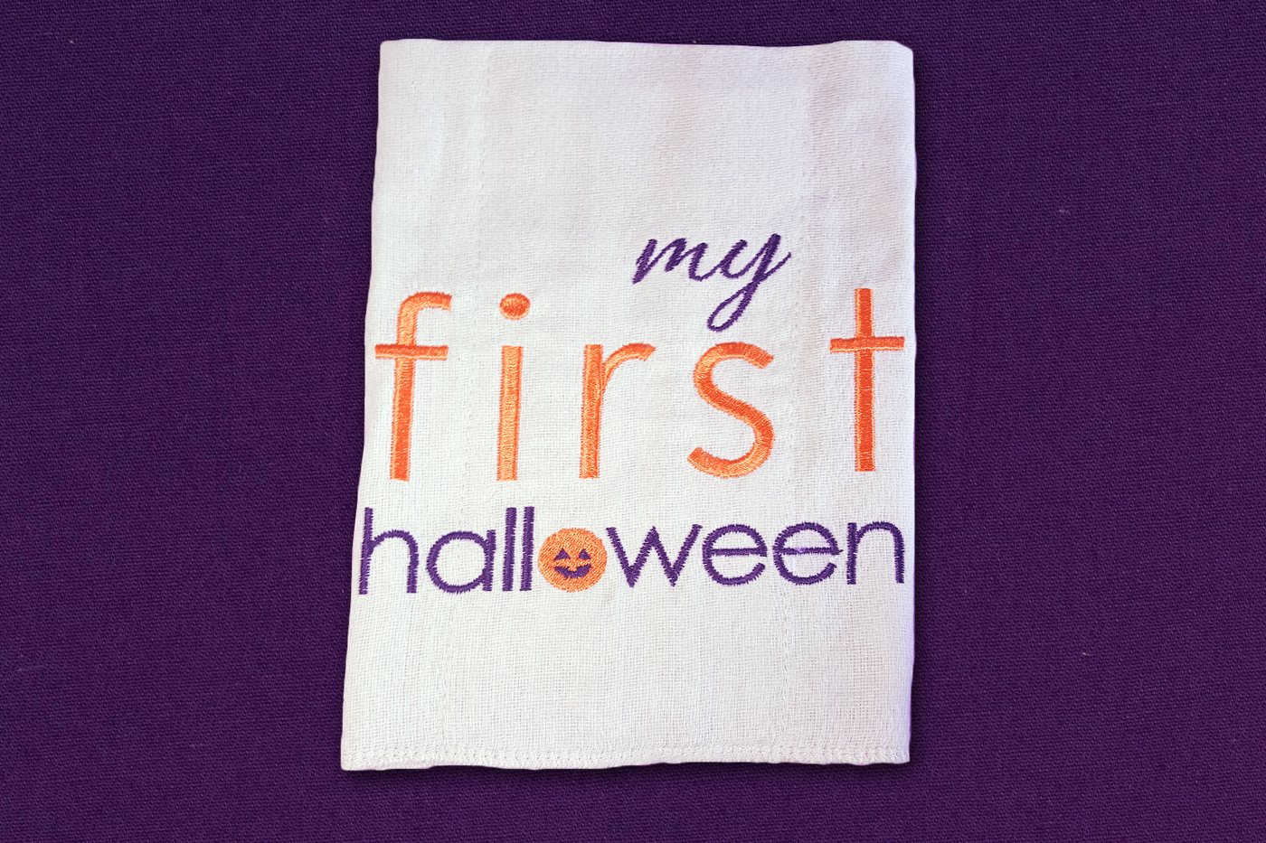 Embroidery design that says "my first halloween." The O has a jack-o-lantern face.