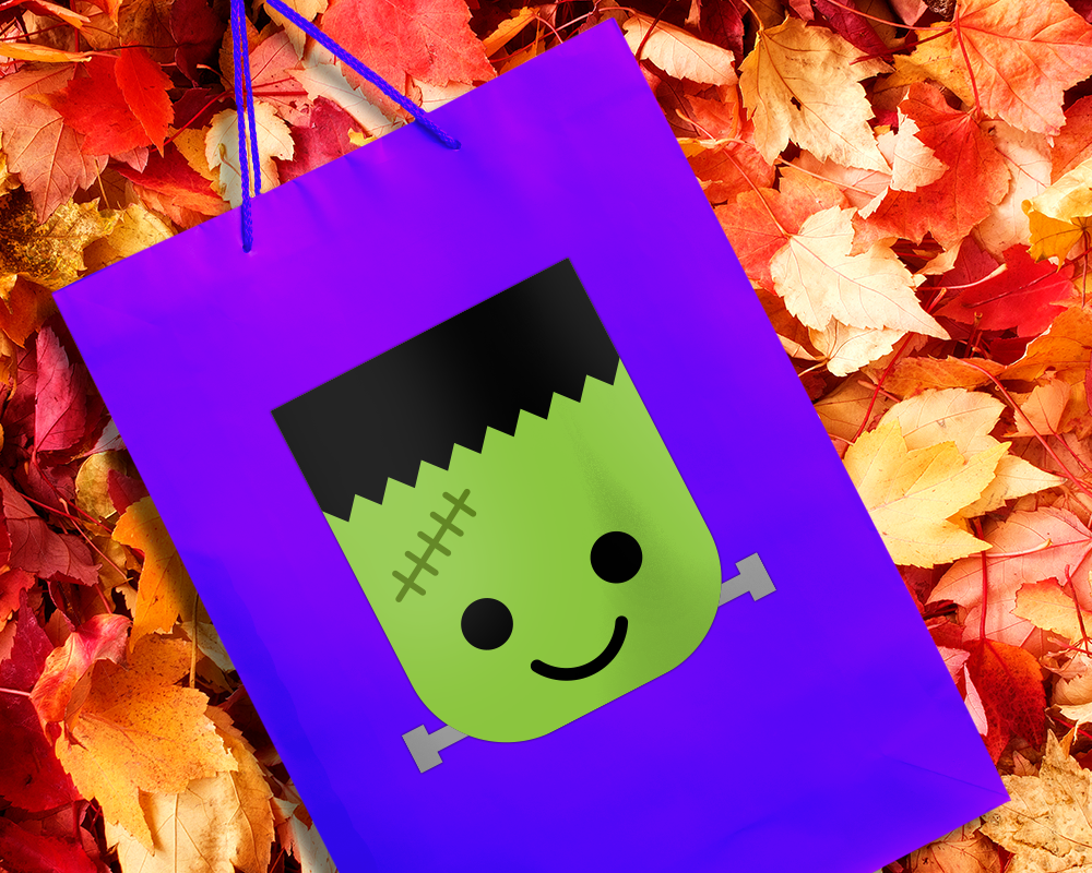Purple bag sitting in fall leaves. On the bag is a cute Frankenstein's monster face.