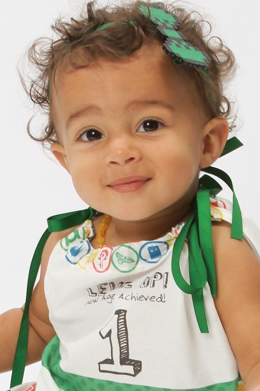 A black baby girl wears a green perler bead bow in her hair.