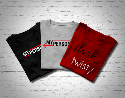 Three folded tees. Two say "My person" with arrows. One has the arrow pointing right, the other has the arrow pointing left. The other design says "dark and twisty."