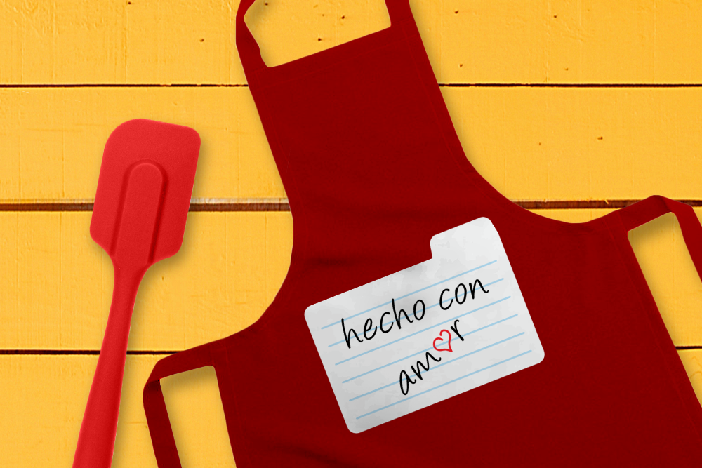 Red apron with a white recipe card design that says "hecho con amor." The o in Amor is a heart.