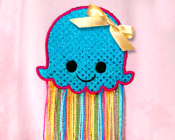 Cute smiling applique jellyfish. A real ribbon has been added and the tentacles are made from multicolored yarn.