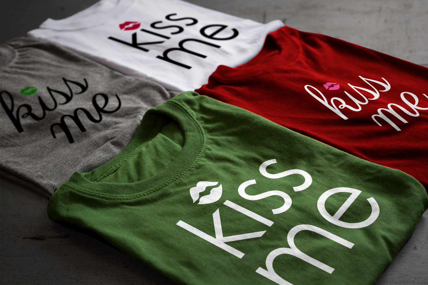 Four folded shirts. Each says "kiss me" with lips dotting the i.
