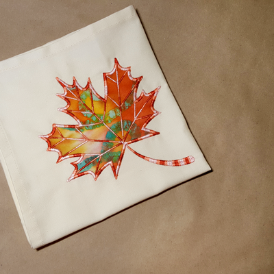 A white napkin with an applique of a maple leaf.
