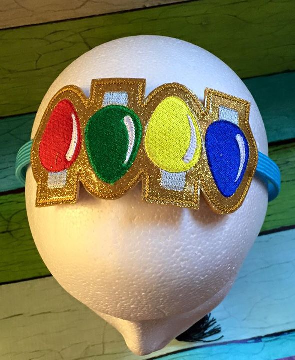 A headband with a slider in the hoop design on top that has 4 Christmas light bulbs in different colors