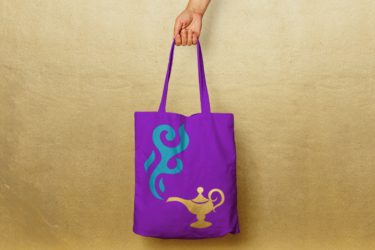 White hand holding a purple tote bag with a magic lamp design.