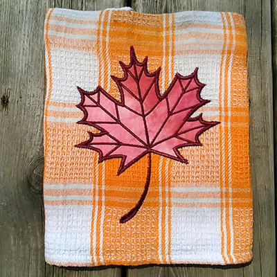 A tea towel with an applique of a maple leaf.