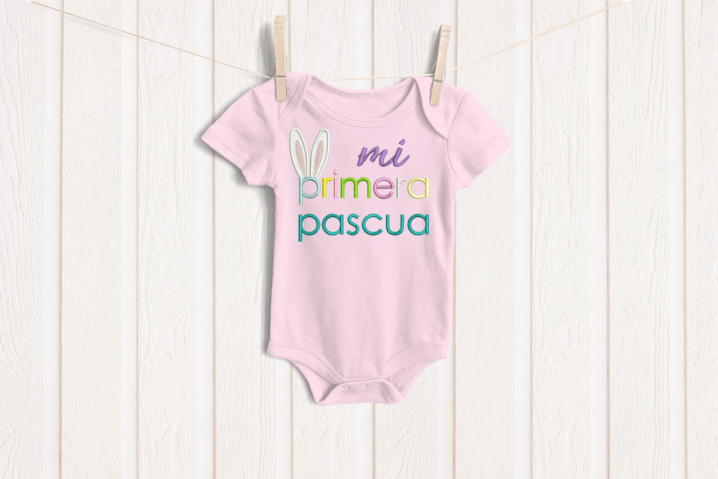 Baby onesie with embroidery that says "mi primera pascua" with rabbit ears on the p