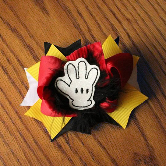 A white feltie of a cartoon glove is added to the center of a red, yellow, black, and white bow with black feather accents.