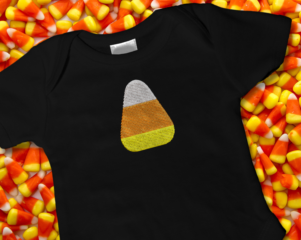 A black baby onesies on a layer of candy corn. The onesie is embroidered with a candy corn in the middle.