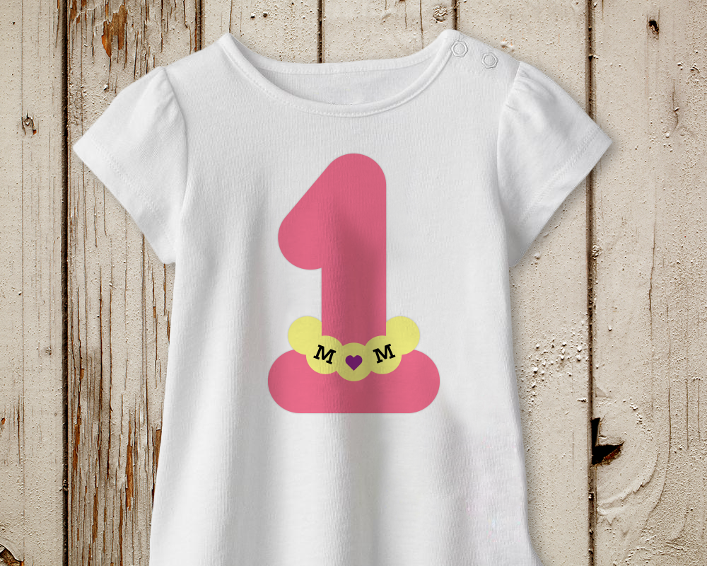 White shirt with a large pink 1. The number has a beaded necklace that says "MOM" with a heart for the O.