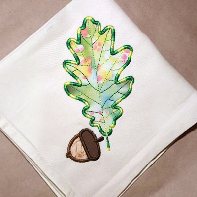 A white napkin with an applique of an oak leaf and acorn.