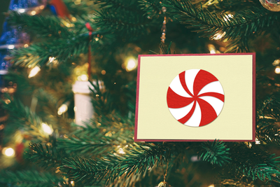 A card nestled in a Christmas tree. On the card is a paper round red and white peppermint.