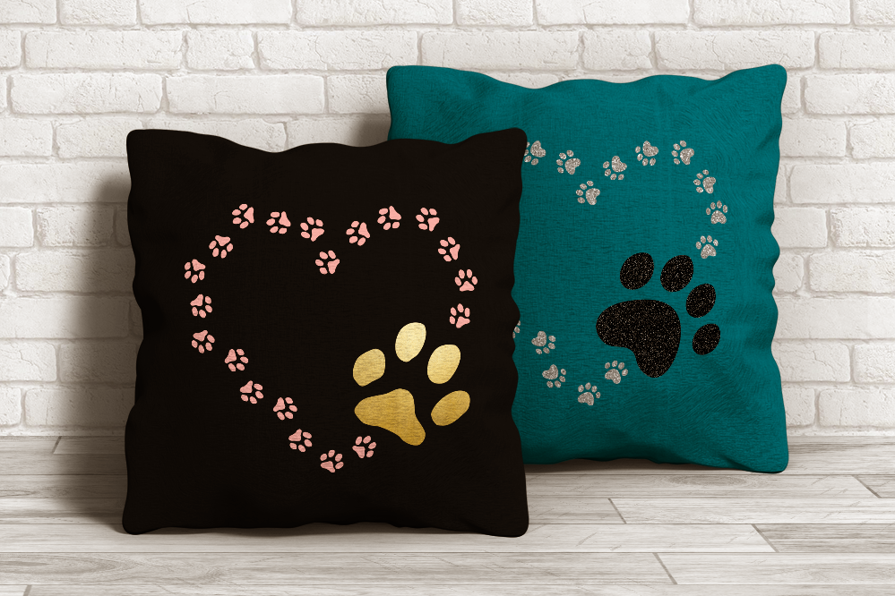 Two throw pillows with a heart made out of paw prints. A larger paw print is at the lower right. One set of prints resembles cat paws, the other looks like dog paws.