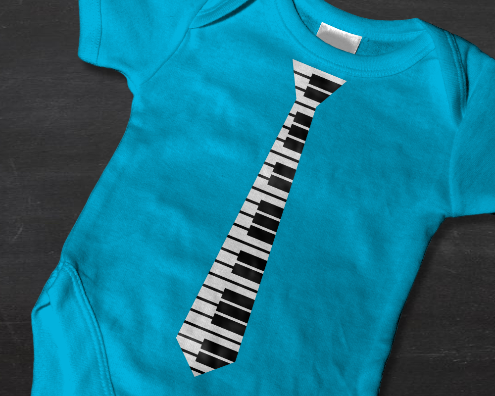 A bright blue baby onesie on a chalkboard background. The shirt has a design that looks like a piano key necktie.